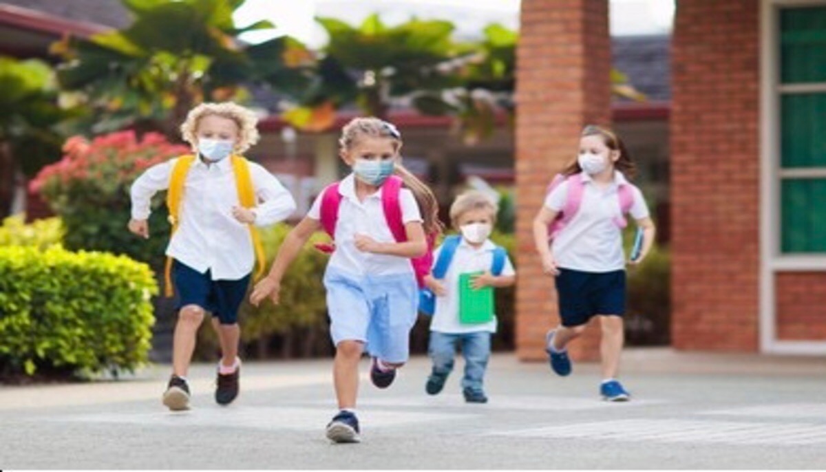 Children running outside a school while wearing masks