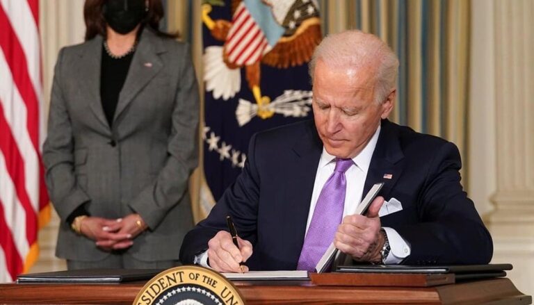 President Joe Biden signs paperwork at his desk