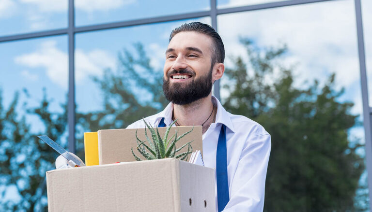 happy businessman with cardboard box with office supplies in hands standing outside office building, quitting job concept