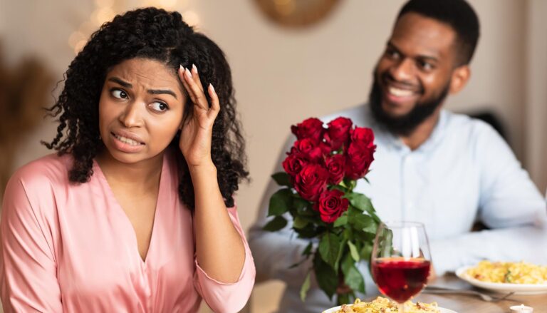 Bad Date. African American Couple Having Unsuccessful Meeting In Restaurant, Funny Disappointed Shoked Black Woman Feeling Embarrassment Covering Face, Man Giving Her Bouquet Of Red Roses