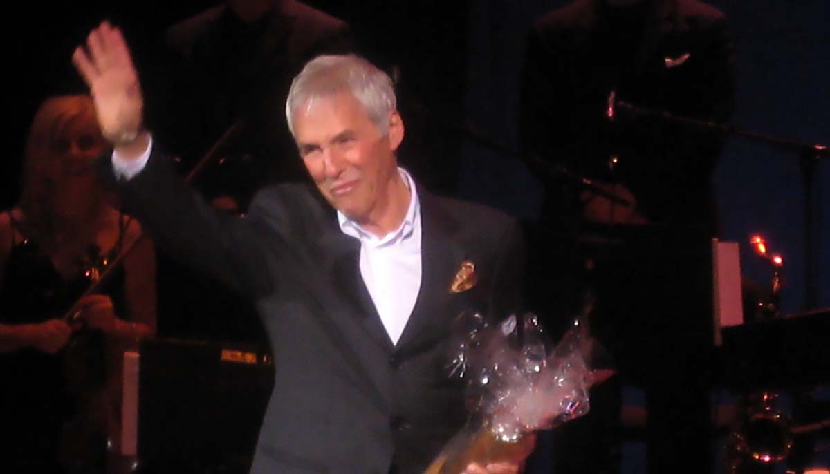 Burt Bacharach holding flowers and waving to the crowd during a performance
