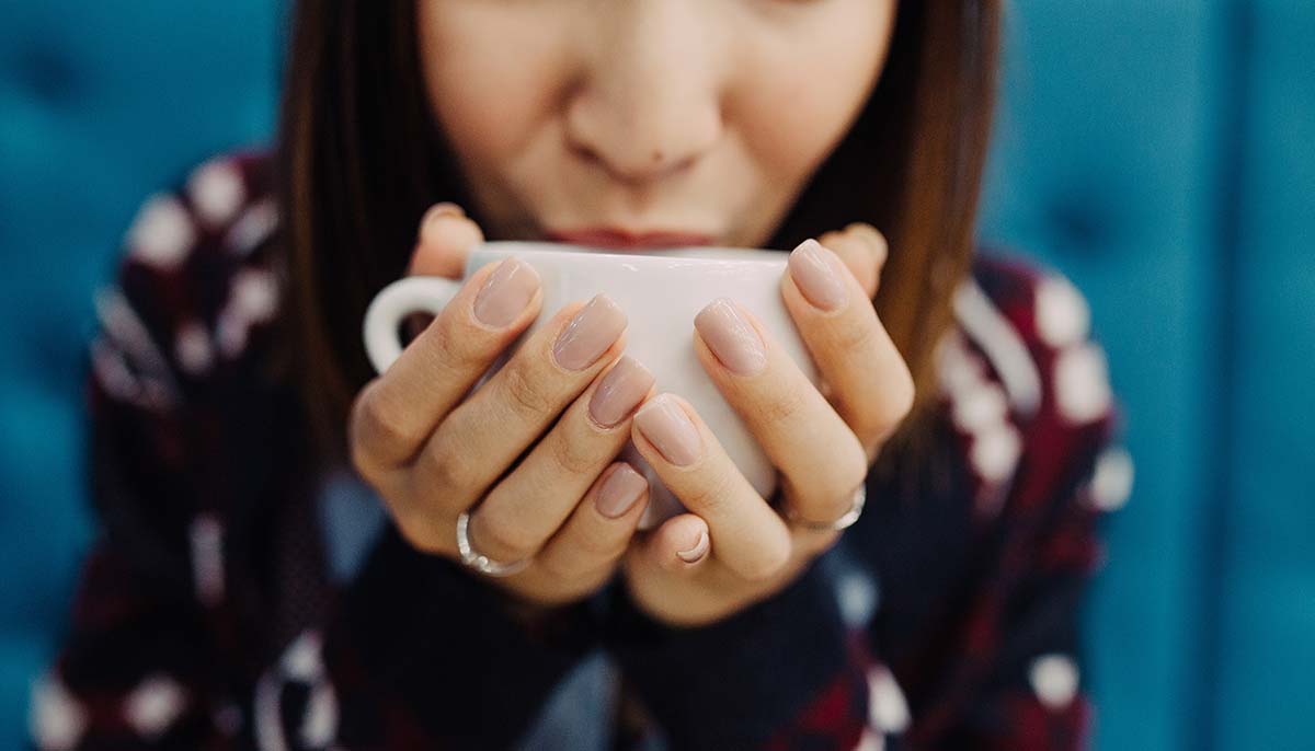 Close-up of a woman's hand holding a cup of hot coffee or tea
