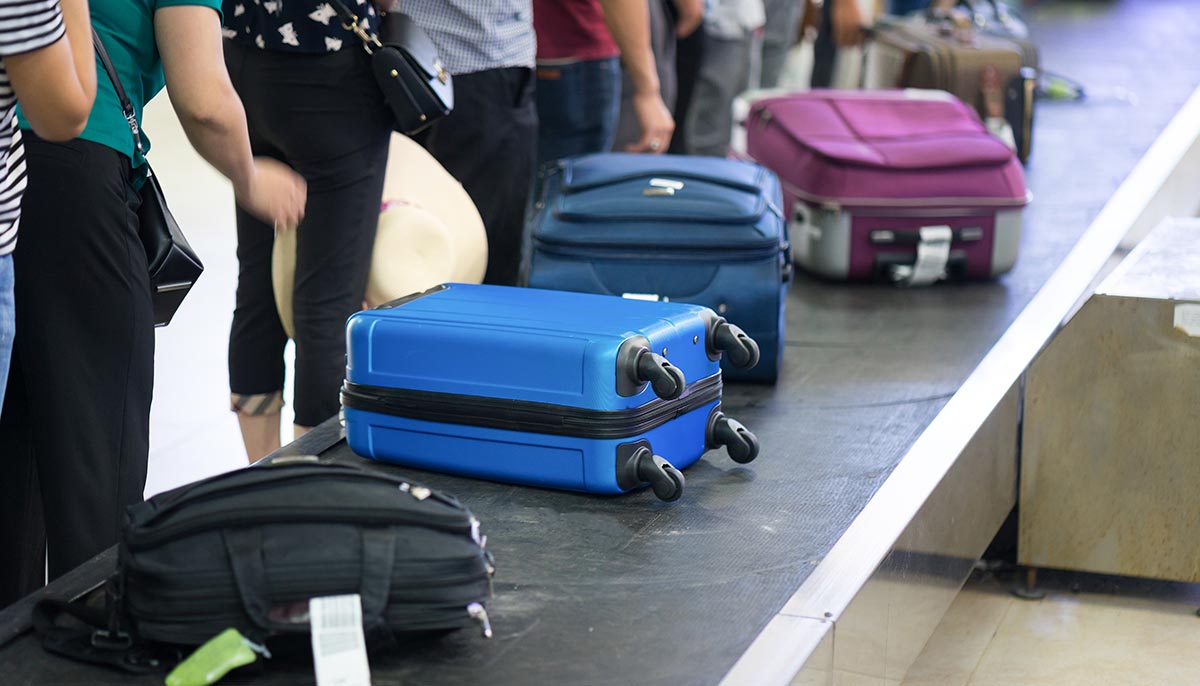 Suitcase on luggage conveyor belt at baggage claim at airport. Lines of people waiting for their baggage