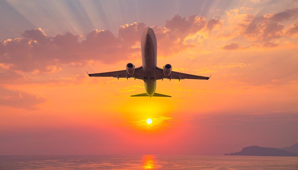 Airplane flying over tropical sea at sunset